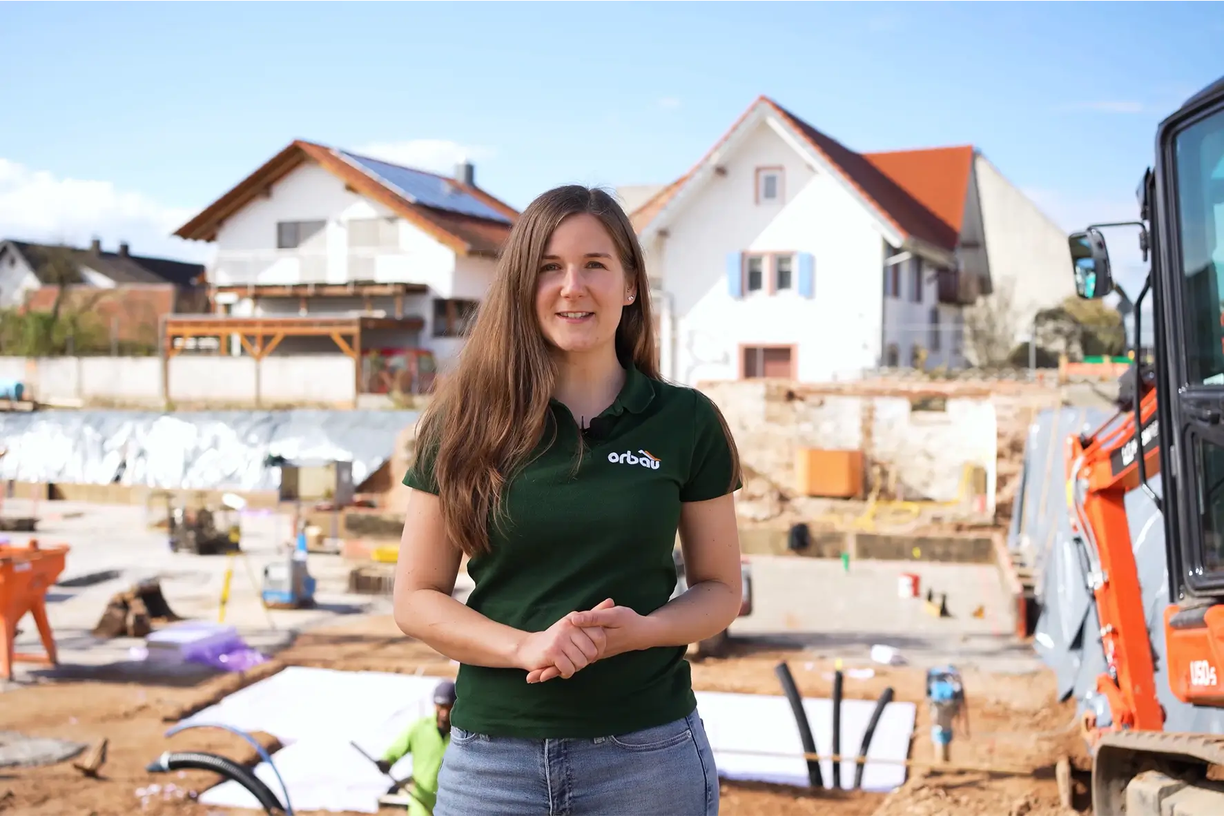 Randi von orbau steht auf einer Baustelle und spricht mit einem Mitarbeiter. Im Hintergrund ist ein Rohbau eines Mehrfamilienhauses zu sehen.