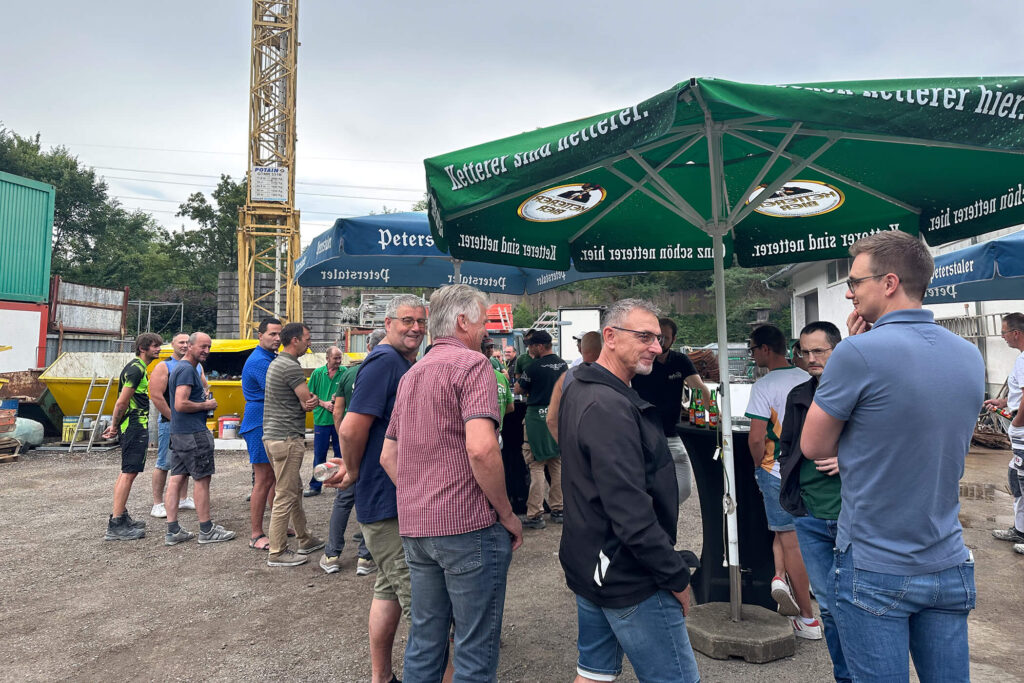 Kollegen beim Sommerfest der orbau Gruppe unter Sonnenschirmen im Gespräch, Gengenbach Bauhof 2025.