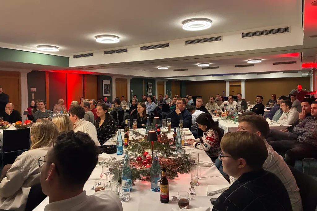 Mitarbeiterinnen und Mitarbeiter sitzen gemeinsam im festlich dekorierten Saal bei der Weihnachtsfeier 2025