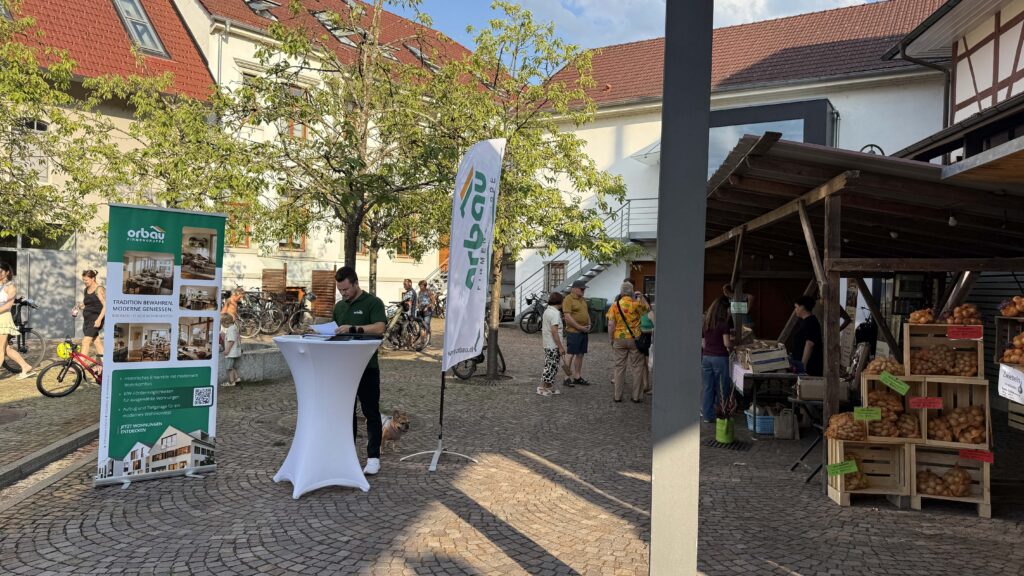 ORBAU-Infostand mit Vertriebsmitarbeiter beim Tavernenabend in Biberach und Roll-up zum Wohnprojekt „Kreuz“.