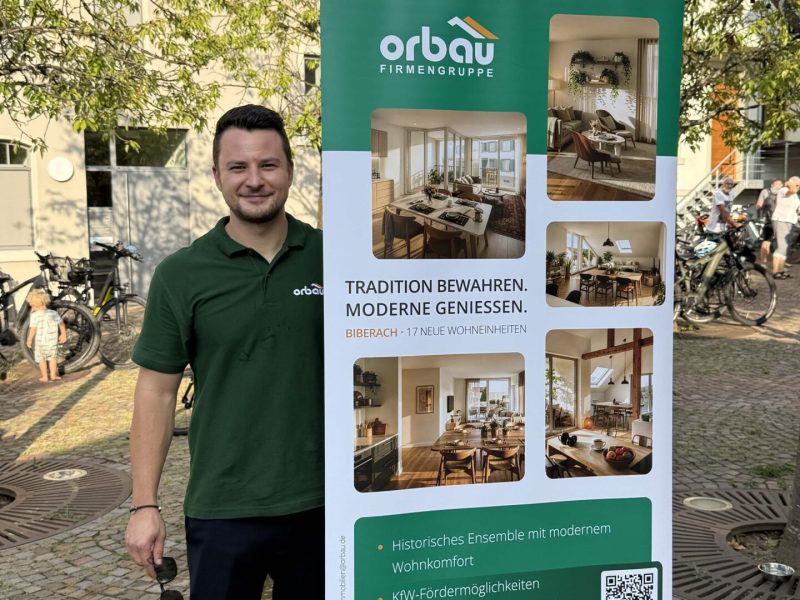 ORBAU-Vertriebsmitarbeiter Julian Fieß neben einem Roll-up zum Wohnprojekt „Kreuz“ beim Tavernenabend in Biberach.