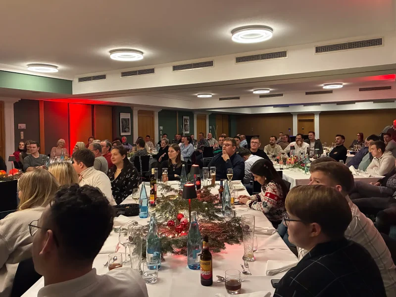 Mitarbeiterinnen und Mitarbeiter sitzen gemeinsam im festlich dekorierten Saal bei der Weihnachtsfeier 2025